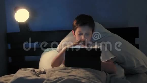 晚上男孩躺在床上用他的数码平板电脑关掉灯睡着了视频的预览图