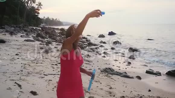 日落时分美丽的年轻黑发女人在热带海滩上玩肥皂泡慢动作1920x1080视频的预览图