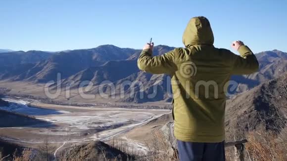 手里拿着电话的人对山顶上美丽的景色感到高兴举起手来视频的预览图