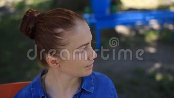 一位身穿牛仔服脸上长着雀斑的红发美女坐在公园的长椅上视频的预览图