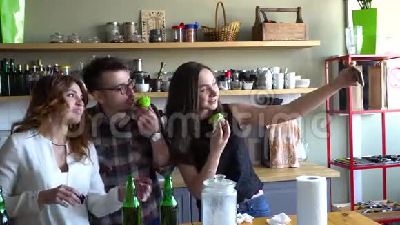 一个男人和两个女孩在厨房里用纸杯蛋糕和啤酒做自拍视频的预览图