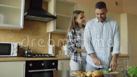在家做早餐的时候快乐的年轻夫妇在厨房里亲吻拥抱和聊天视频的预览图