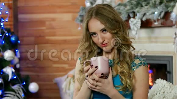 一位美女欣赏热饮杯的肖像女人手拿咖啡或茶杯对抗舒适的壁炉视频的预览图