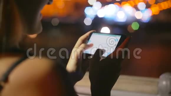 屋顶智能手机上的年轻女性短信特写镜头以应对明亮的夜景视频的预览图