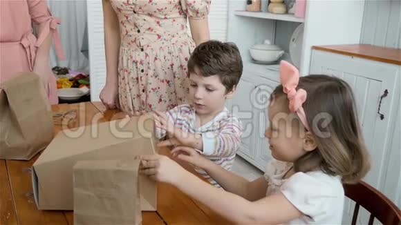 带礼盒的快乐孩子早上男孩和女孩打开盒子厨房里放着糖果家庭早餐快乐视频的预览图