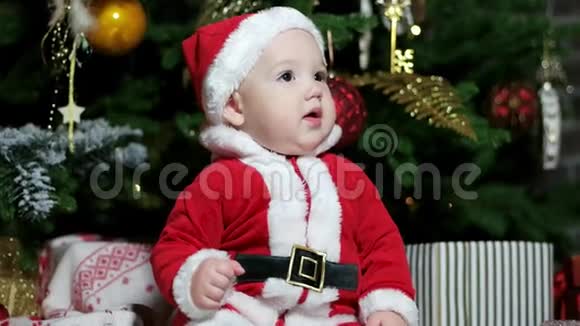可爱的男孩在圣诞树附近玩耍穿着圣诞老人服装的小婴儿穿着狂欢节服装的孩子在家里玩耍视频的预览图