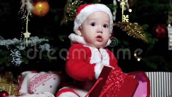 圣诞礼物在一个孩子手里他穿着圣诞老人的服装可爱的男孩坐在圣诞树附近孩子在里面视频的预览图