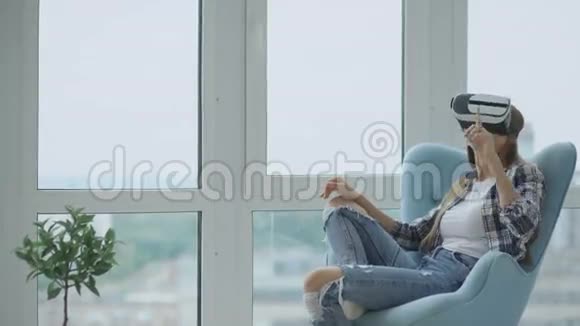 年轻女性使用虚拟现实耳机坐在阳台上的椅子上有VR体验视频的预览图