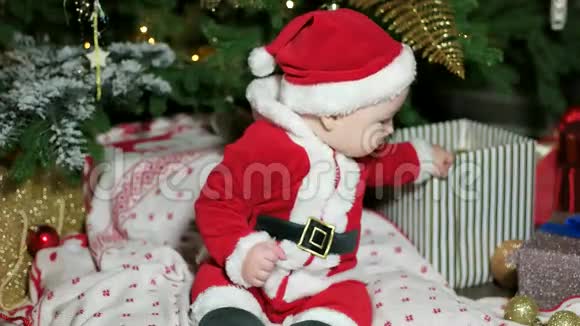 穿着圣诞老人服装的小宝宝在圣诞树附近玩耍的可爱男孩穿着狂欢节服装的孩子在家玩耍视频的预览图