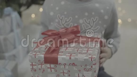 近距离观看兴奋的孩子快乐的男孩打开圣诞礼物盒惊讶地坐在新年树附近视频的预览图