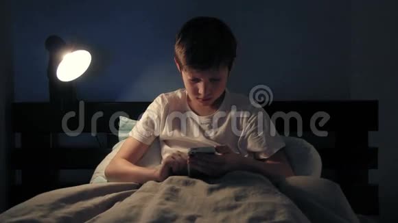 男孩晚上躺在床上用智能手机睡着了视频的预览图