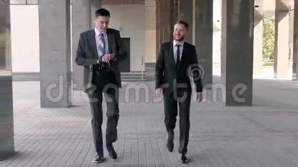 两个英俊的商人在沿着办公楼散步时在一起聊天视频的预览图