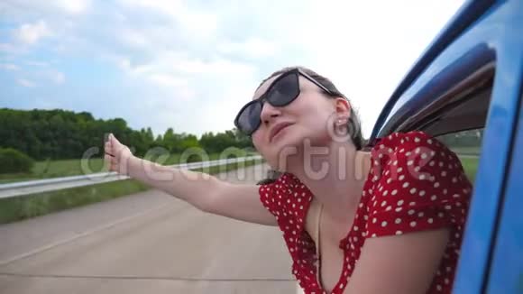 戴着太阳镜的快乐女孩斜靠在老式车窗外享受旅行年轻女子望着窗外移动视频的预览图