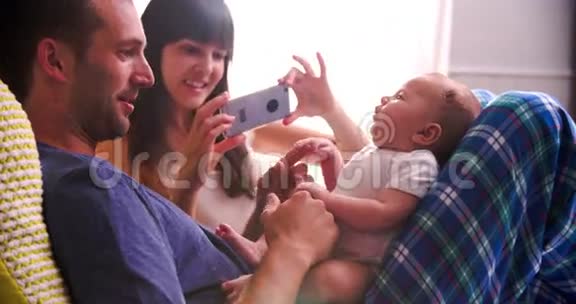 在床上为新生儿女儿拍照的父母视频的预览图