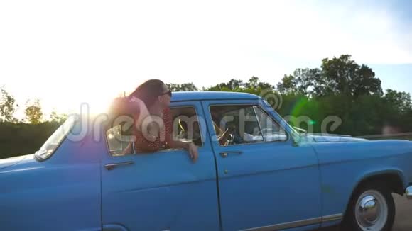 戴墨镜的快乐女孩斜倚在复古车窗外享受旅行年轻女子望着窗外移动的老人视频的预览图