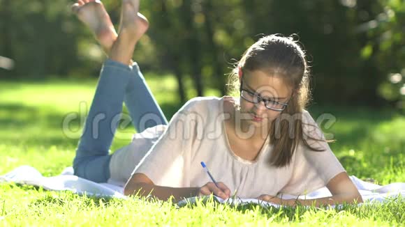 草地上年轻漂亮的女孩写笔记本视频的预览图