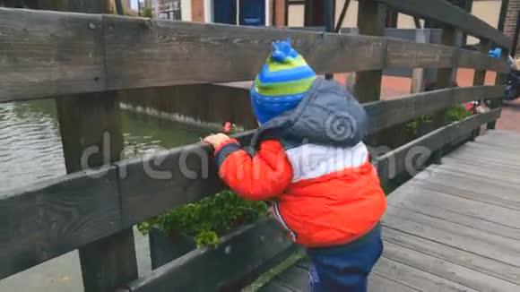 寒冷的日子里可爱的小男孩站在木桥上看着河视频的预览图