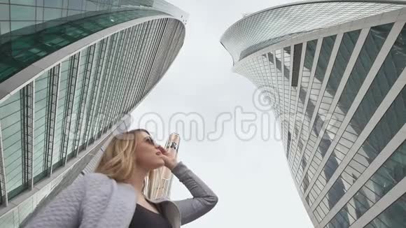 一个金发女孩走着欣赏市中心的摩天大楼和高层建筑慢动作射击视频的预览图