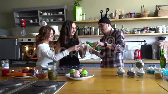 两个女孩和一个戴着疯狂帽子的男人在厨房庆祝生日并在厨房里用香槟庆祝生日视频的预览图