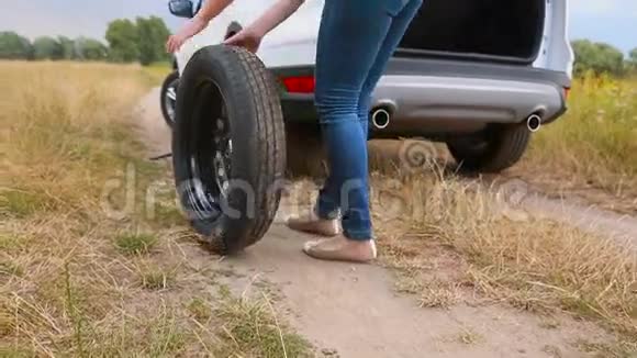 一位年轻女子在乡间的锉刀上滚动汽车备用车轮视频的预览图