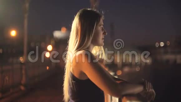 夜晚站在屋顶上看城市的美丽年轻女子的画像视频的预览图