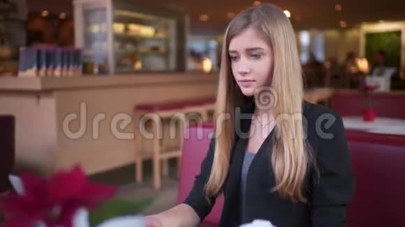 那个穿着黑色夹克的金发女郎坐在咖啡馆A里她喝了咖啡和她一起工作视频的预览图