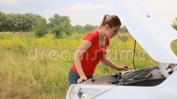 年轻的心烦意乱的女人打开破车的引擎盖看着引擎视频的预览图