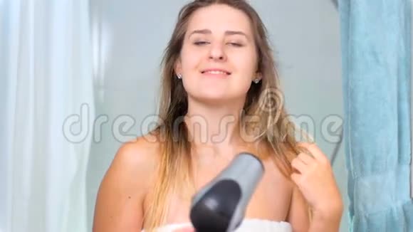 带着微笑的金发女人在浴室用吹风机的慢镜头视频的预览图