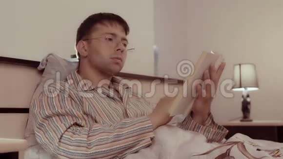 年轻的帅哥在睡觉前翻阅他的书视频的预览图
