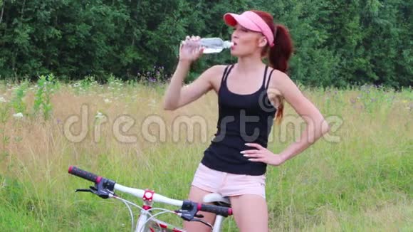 戴帽子的女骑自行车在森林里夏天喝纯净水视频的预览图