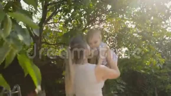 年轻微笑的母亲把她的小儿子举到公园树下视频的预览图