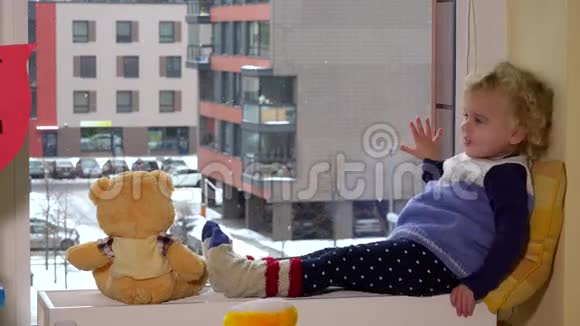 可爱的孩子和最好的朋友泰迪熊坐在窗户附近下雪了视频的预览图