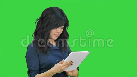 微笑着年轻女子在绿色屏幕上的平板电脑上工作Chroma键视频的预览图