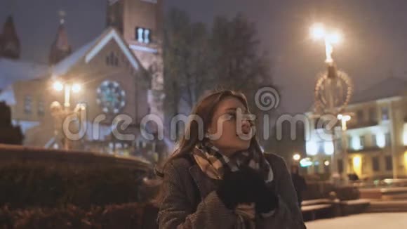 晚城背景下的一个年轻女孩温暖了双手在城市的灯光下下雪视频的预览图