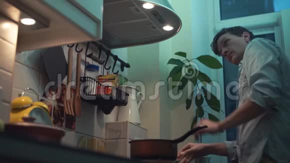 男人在厨房的炉子上用锅做饭用智能手机视频的预览图
