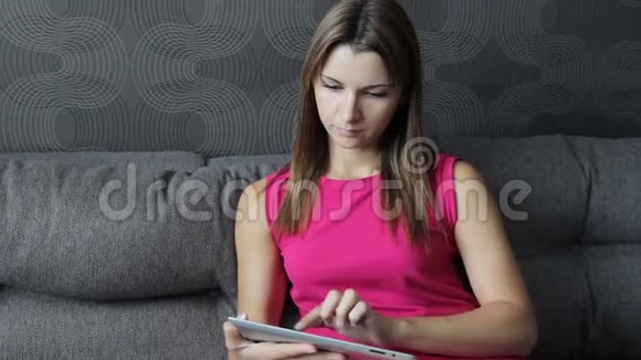 穿裙子的女人坐在沙发上用平板电脑坐在沙发上用平板电脑工作的女孩视频的预览图