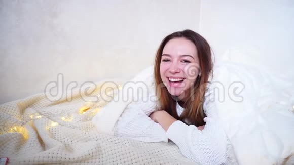 幸福的女人看着相机微笑着躺在地板上被毯子覆盖在花环旁边的明亮房间里视频的预览图
