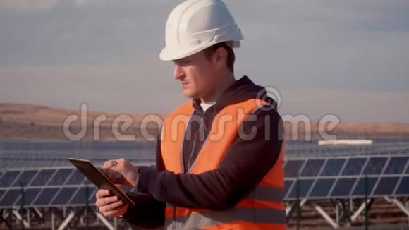 一个戴着头盔的人在一家太阳能发电厂的背景下拿着一平板电脑视频的预览图