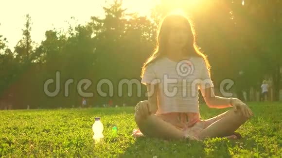 苗条的黑发女孩坐在公园的草地上在烈日下放松4K视频视频的预览图