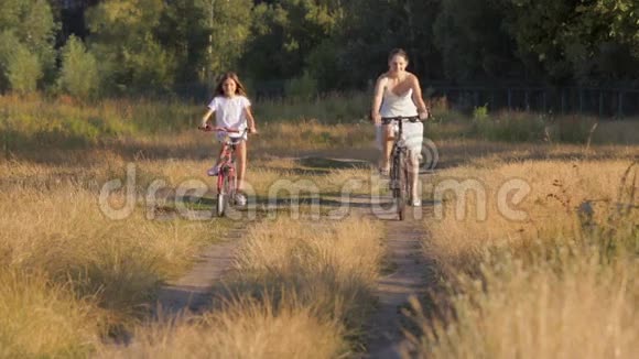 美丽的年轻女子和女孩骑自行车在农村的田野美丽的年轻女子和女孩骑自行车在农村视频的预览图