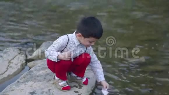 美丽的小男孩让纸船在河上视频的预览图