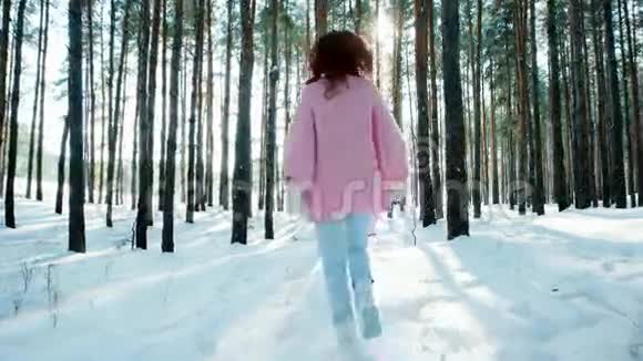 快乐的年轻女子在冬天的森林里在雪地里奔跑在树林里背光穿过树林视频的预览图