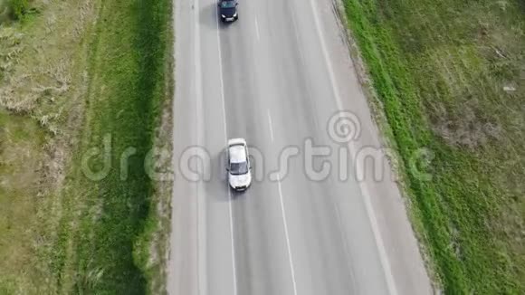 在阳光明媚的一天从无人驾驶飞机上俯瞰沿着空旷的乡村道路行驶的汽车视频的预览图
