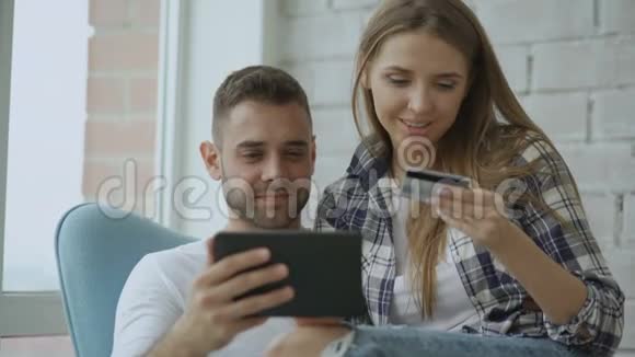 年轻的情侣们用数码平板电脑上网购物坐在现代阁楼公寓的阳台上视频的预览图