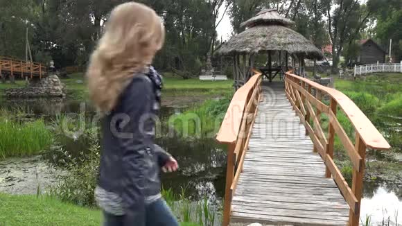 妇女步行到桥上的木树穿过公园的水槽河4K视频的预览图