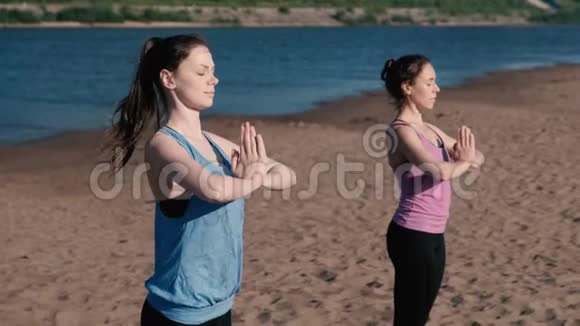 两个女人站在城市河边的海滩上伸展瑜伽美丽的城市景色令人讨厌的姿势视频的预览图