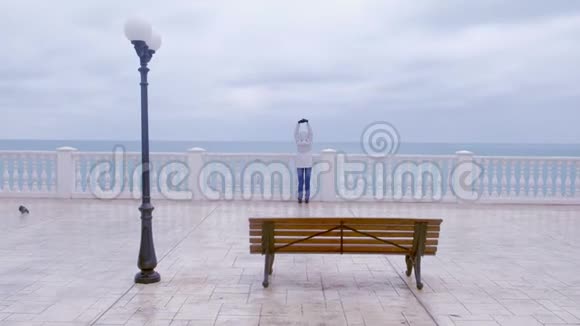 穿着白色夹克和引擎盖的女人在美丽的露台上海景在海滨后景视频的预览图