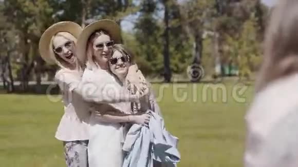 三个戴着太阳镜的年轻女人拥抱在一起玩得开心然后拍照视频的预览图