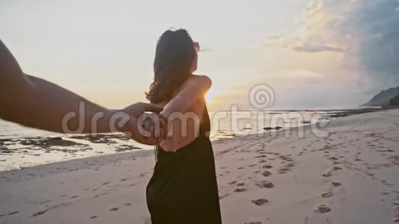 年轻夫妇牵着手女人带领男朋友在空滩上走向日落POV旅游理念视频的预览图