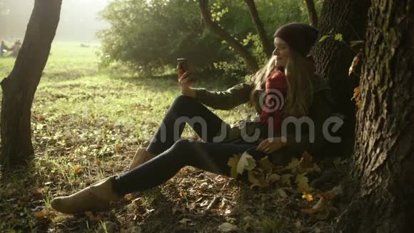 开朗时尚的少女在秋季公园通过电话拍照视频的预览图